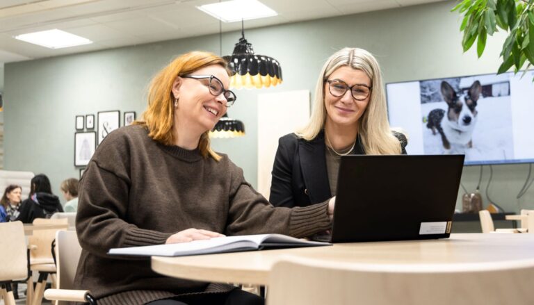 Kaksi naista katsoo hymyillen toimistossa tietokoneruutua.