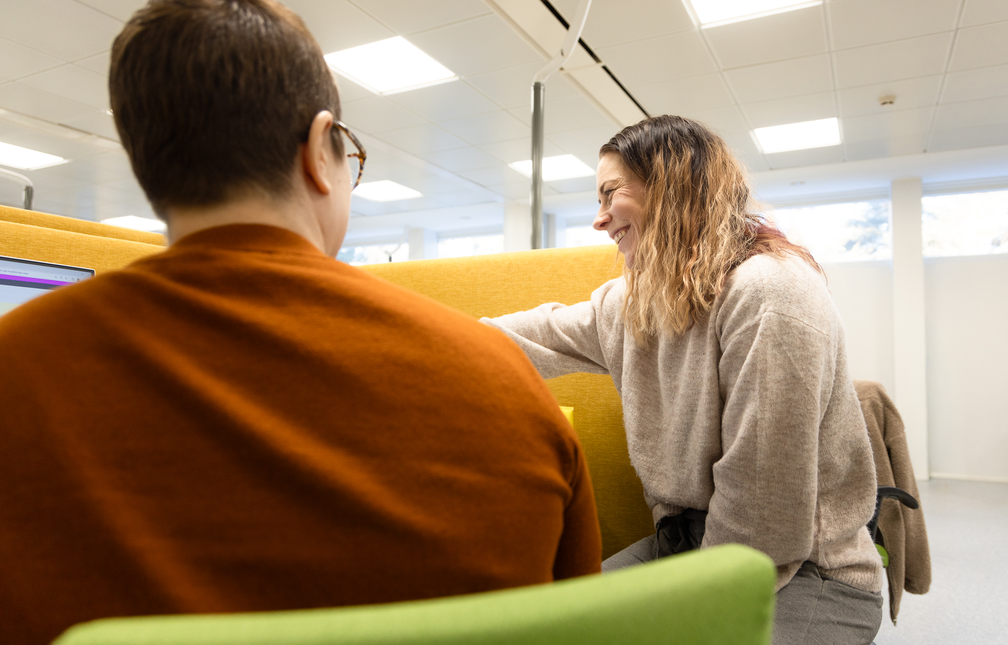 Selin kameraan oleva henkilö ja sivuttain oleva hymyilevä henkilö juttelevat